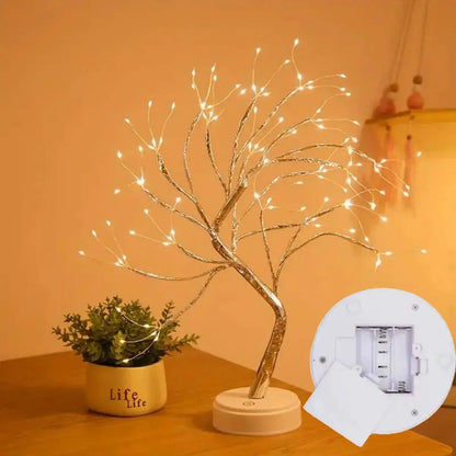 Decorative LED tree with a small plant on a wooden surface, against an orange wall.