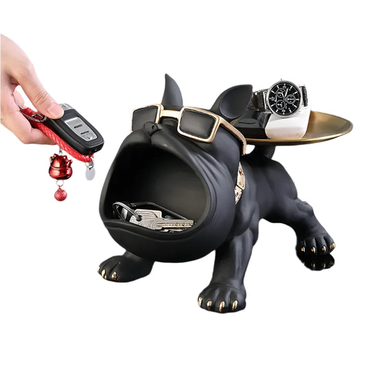 Black dog-shaped key holder with a hand placing keys inside, on a dark surface.